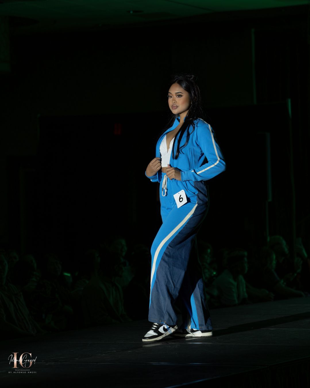 Person models blue tracksuit ensemble on dimly lit catwalk.