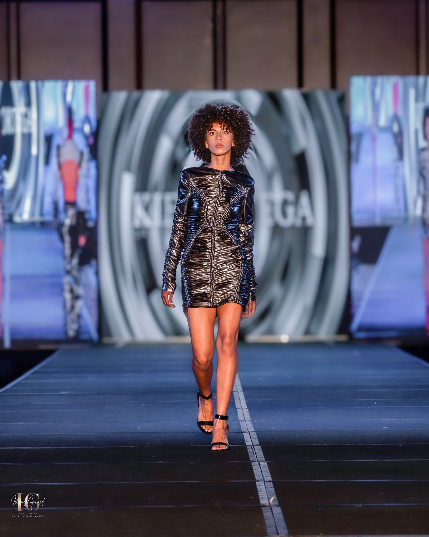 Model presents fitted metallic mini dress with long sleeves on fashion runway.