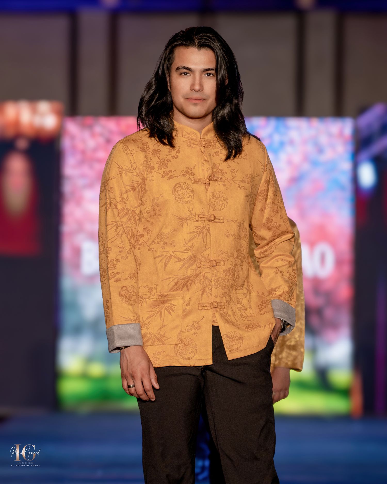 Model wears caramel-colored mandarin collar jacket with dark pants on fashion runway.