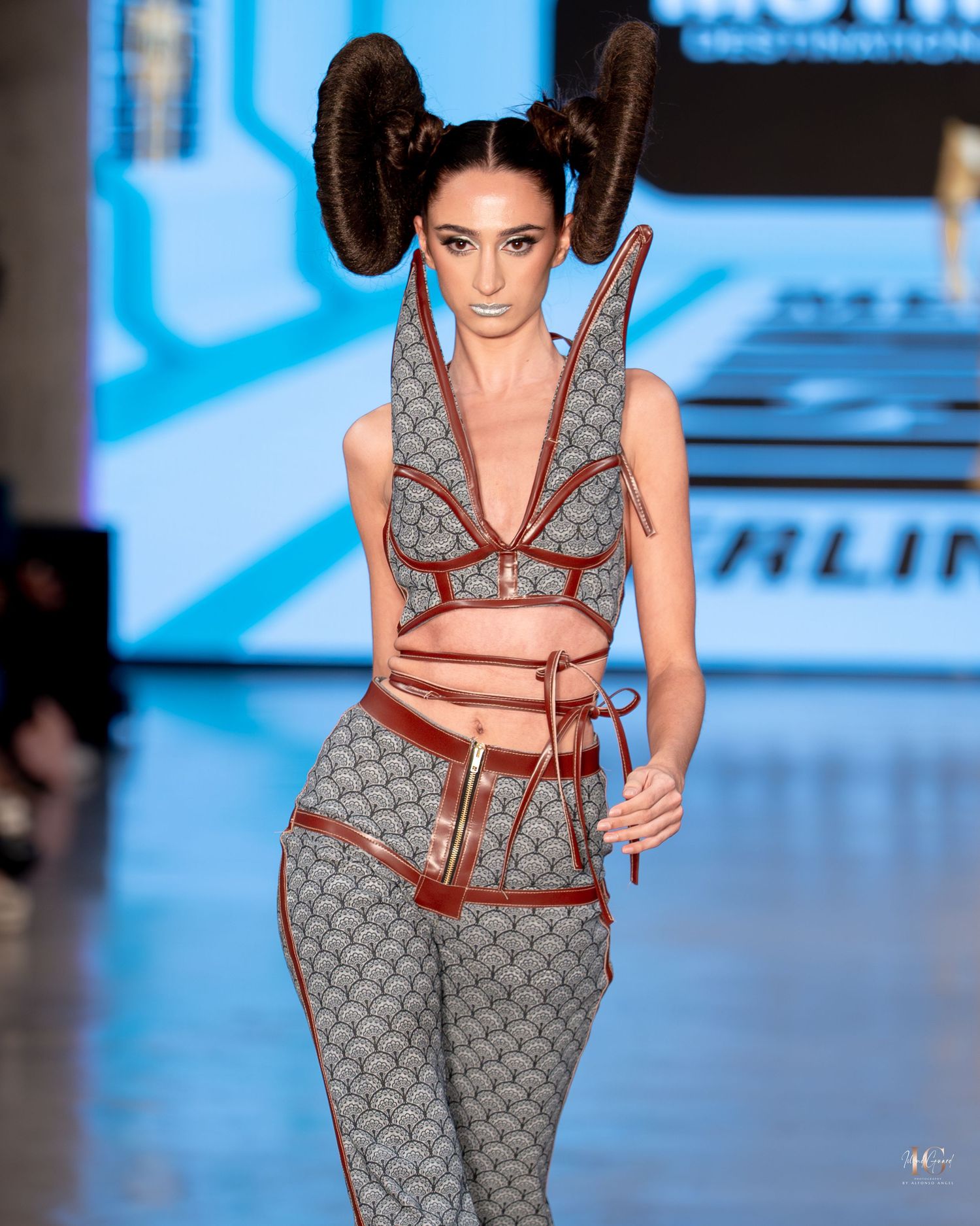 Fashion model walks runway wearing avant-garde Louis Vuitton monogram print outfit with dramatic hair styling at fashion show.