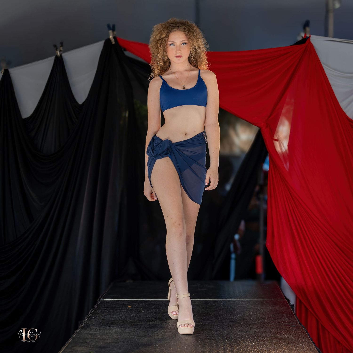 Fashion model showcases blue activewear ensemble on runway with dramatic backdrop.