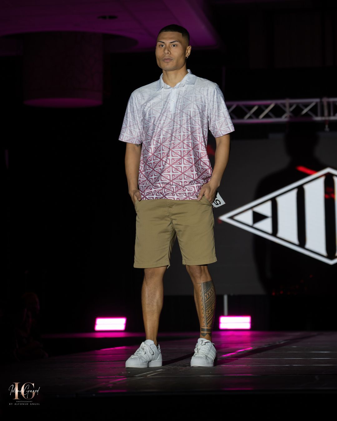 Model wearing gradient white polo and khaki shorts poses on fashion runway.