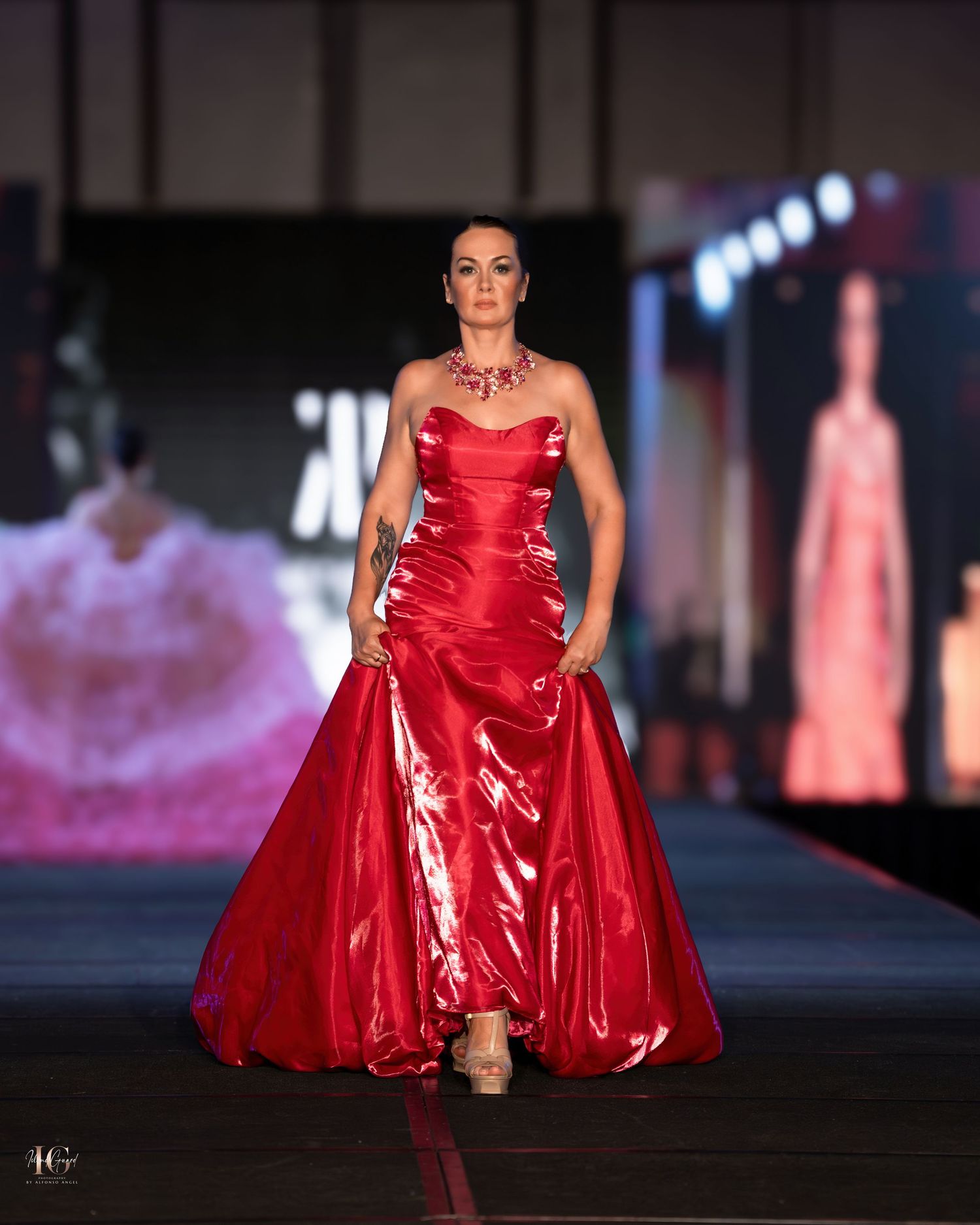 Glamorous red satin evening gown with dramatic silhouette on fashion runway.