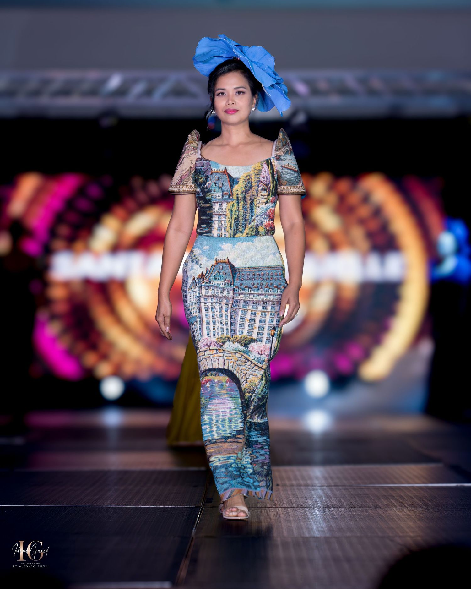 Traditional-inspired dress with patchwork patterns and large blue hat accessory on fashion runway.