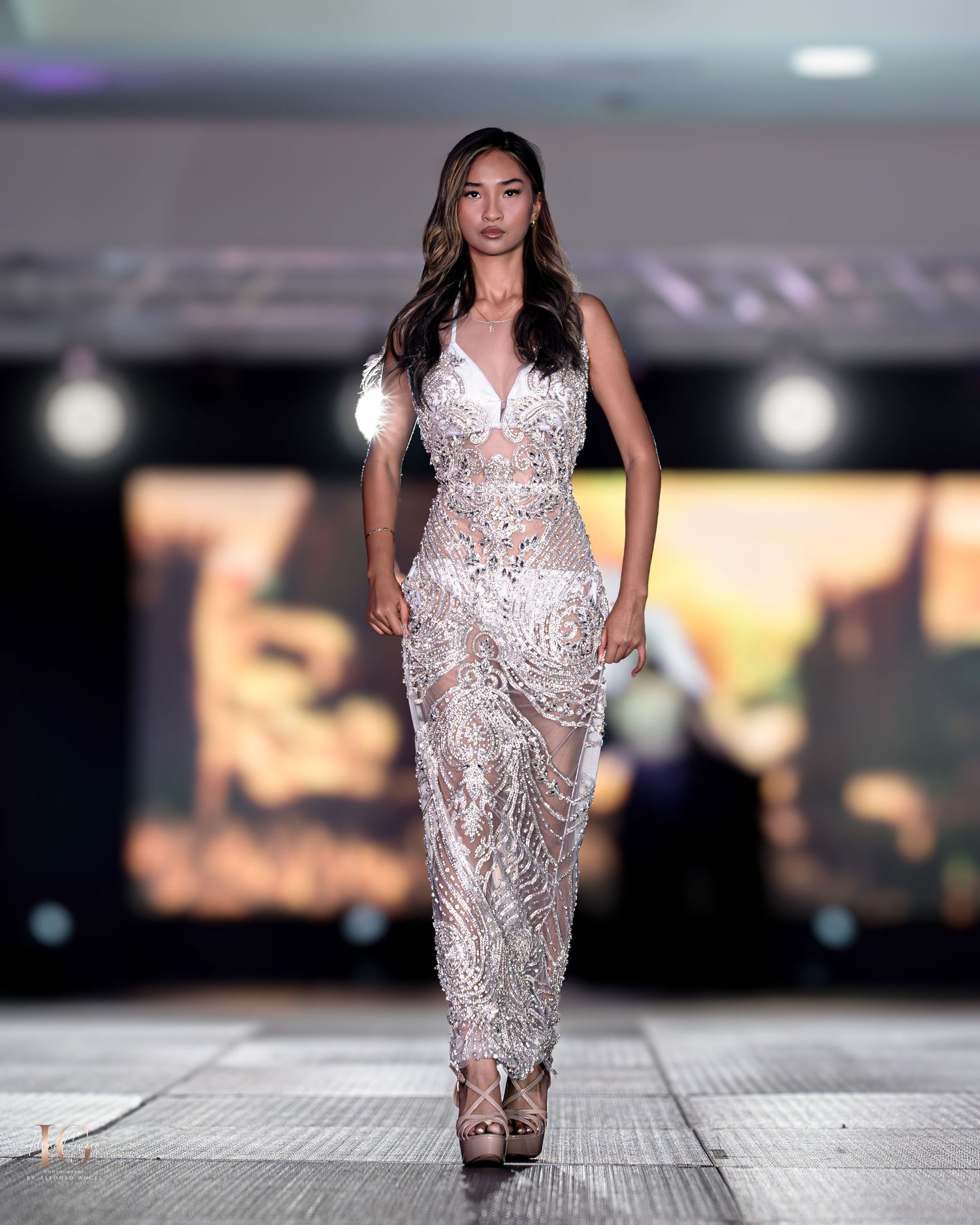 Stunning beaded white evening gown sparkles under runway lights at fashion show.