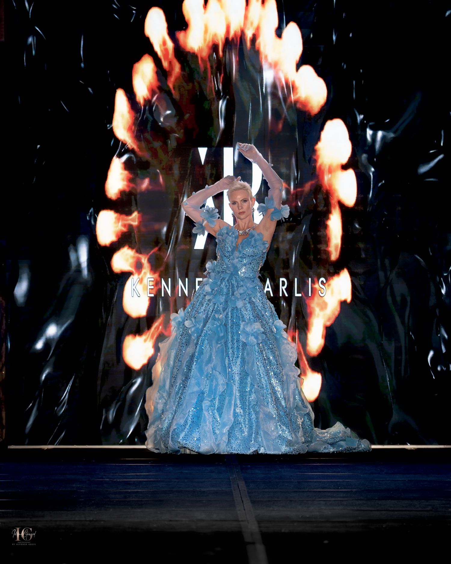 A ethereal blue ballgown glows under dramatic stage lighting with sparkling effects creating a magical performance atmosphere.