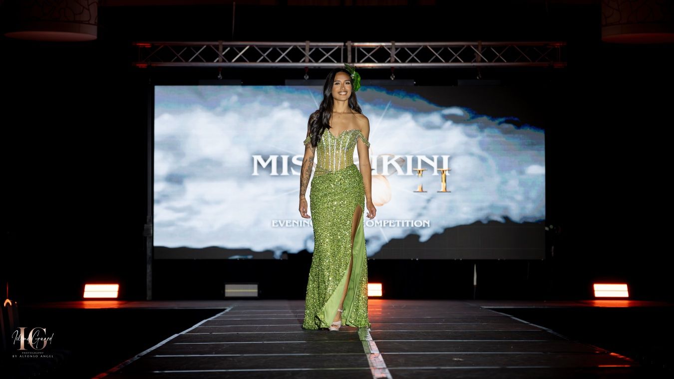 Model walks down a dark runway in a sparkling green sequin gown during a fashion show.