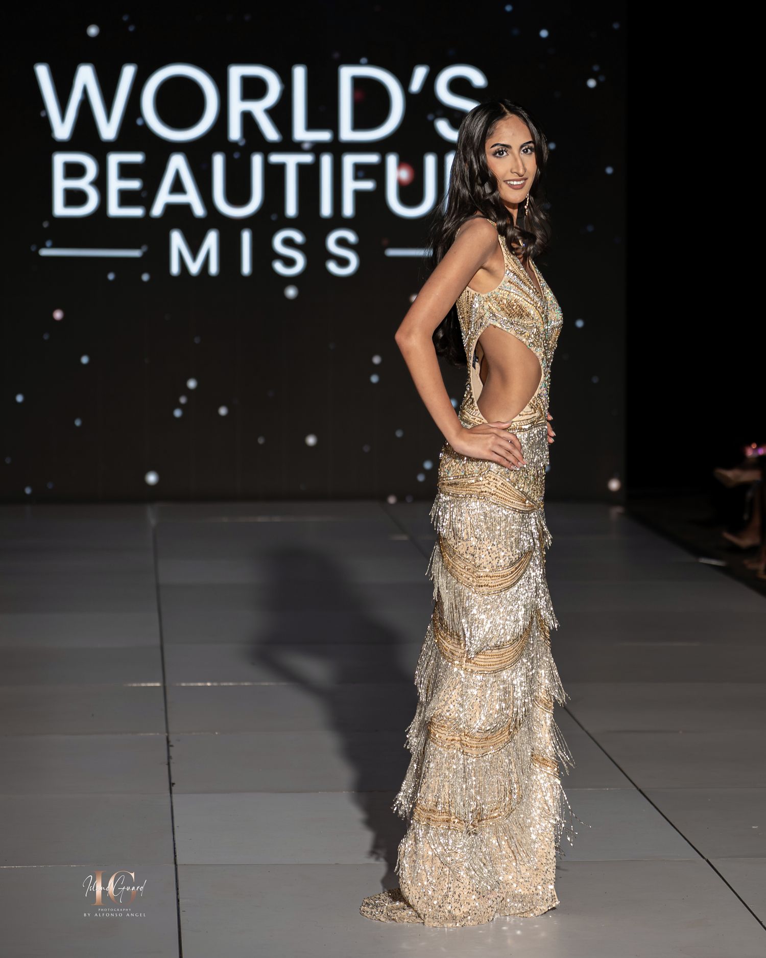 A model walks the runway wearing a shimmering beige evening gown with cutout details at a fashion show.