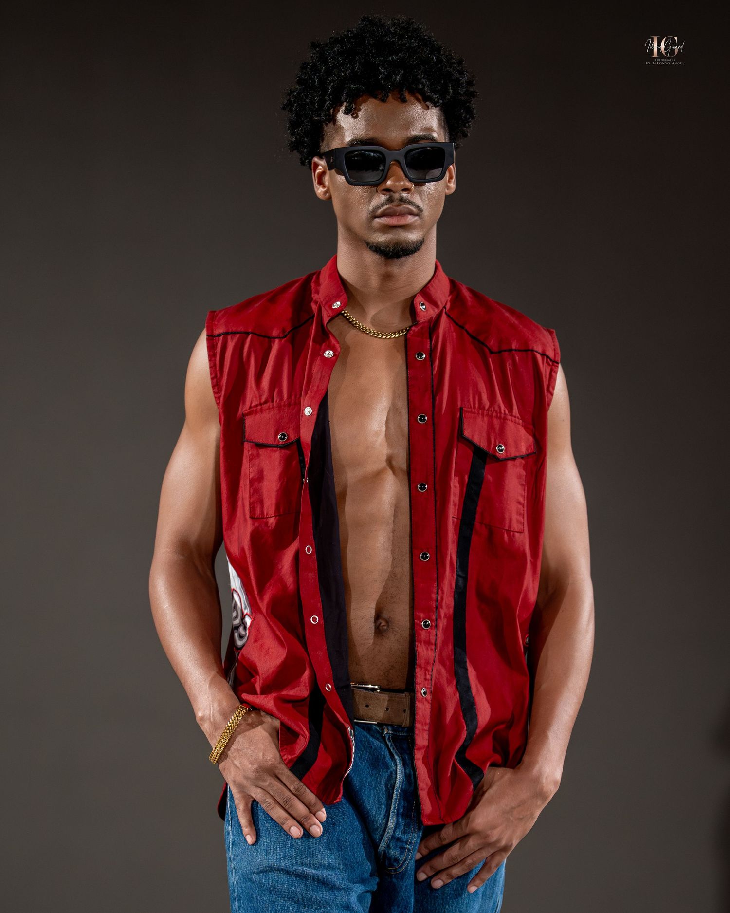 A person in a red sleeveless vest and blue jeans poses against a dark background in a fashion photoshoot series.
