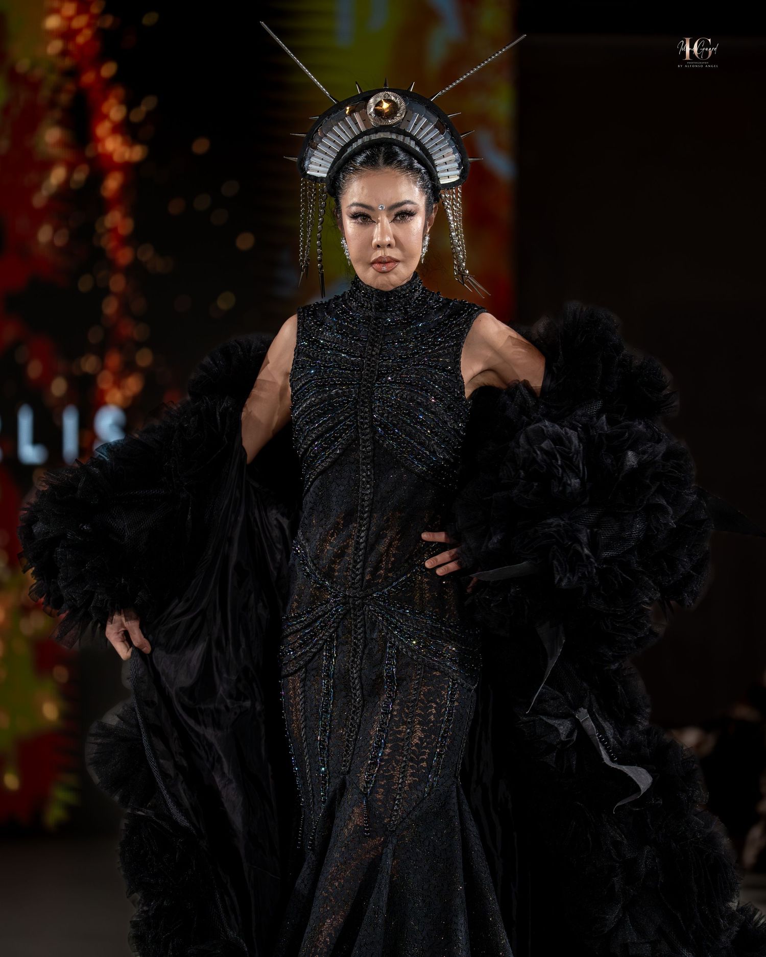 A model walks the runway in an avant-garde black feathered gown with dramatic headpiece at a fashion show.