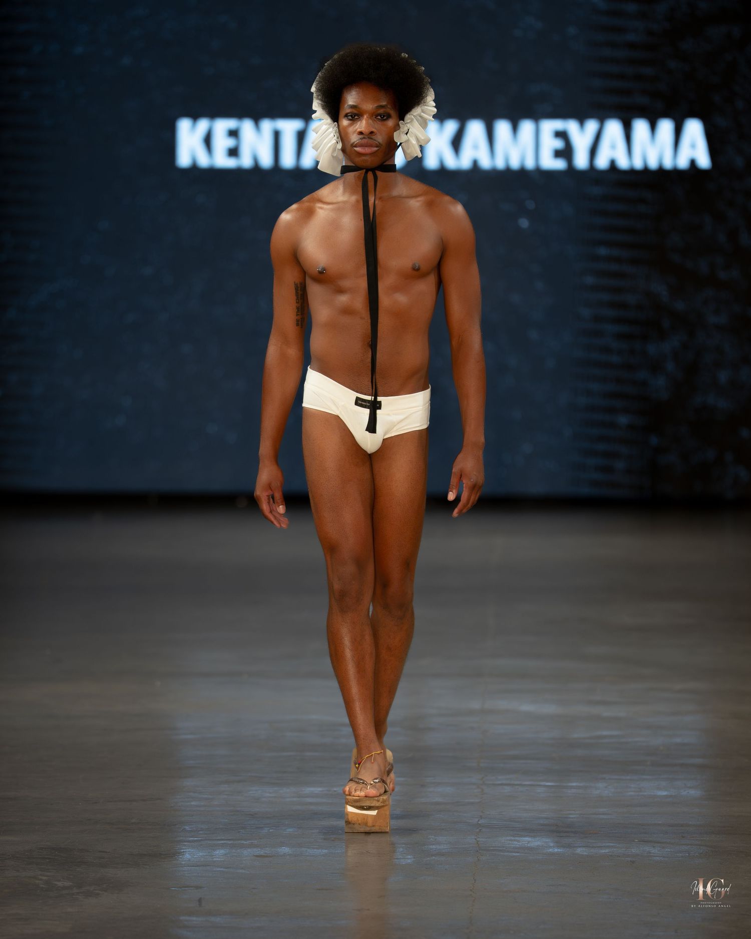 A model walks the runway in white swimwear and sandals during a fashion show for Kenta Kameyama collection.