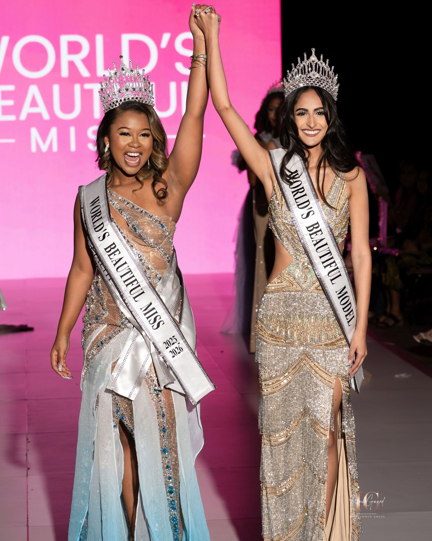 Beauty pageant contestants in sparkly evening gowns wave and smile while walking the runway with a pink backdrop.