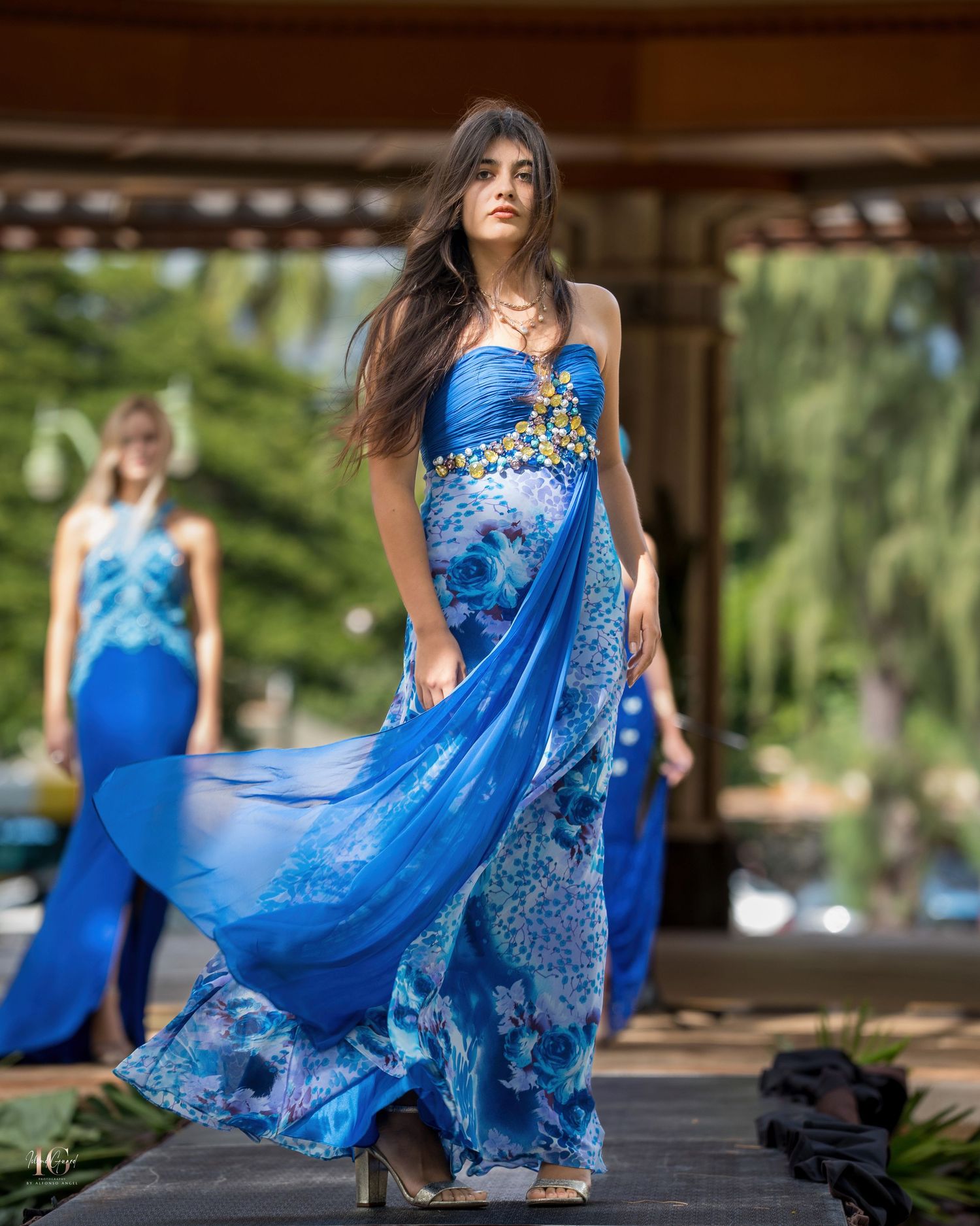 A dancer in a flowing blue dress performs graceful movements in a covered outdoor space.