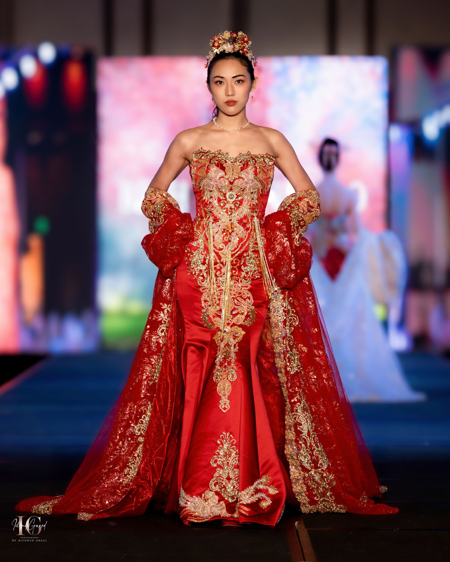 Red and gold embroidered ball gown with matching cape showcased on fashion runway.