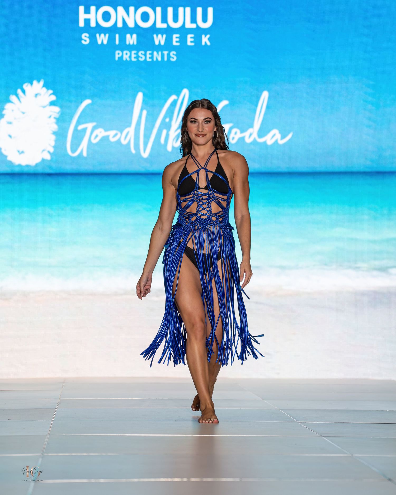 Royal blue fringed swimwear with geometric top design presented at beachside fashion show.