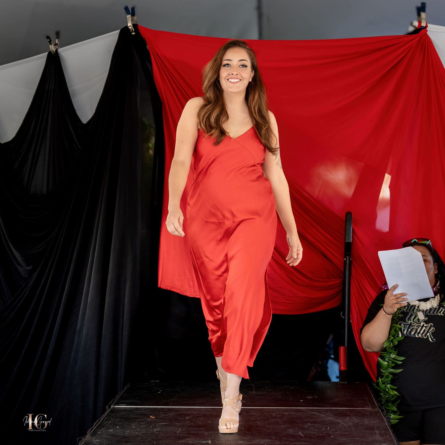 Fashion model in red dress poses against black backdrop in glamorous photo series.