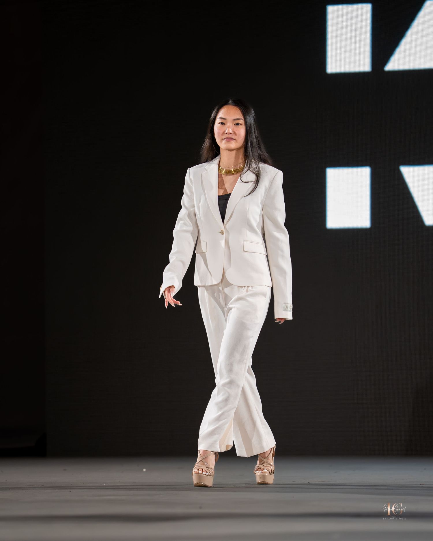 A dancer in a white blazer performs a dynamic movement sequence on a dark stage with dramatic lighting.