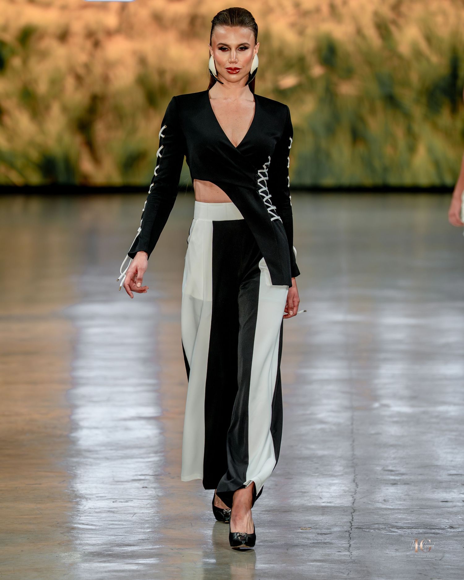 A model walks the runway in a black and white asymmetrical dress with a dramatic side slit during a fashion show.