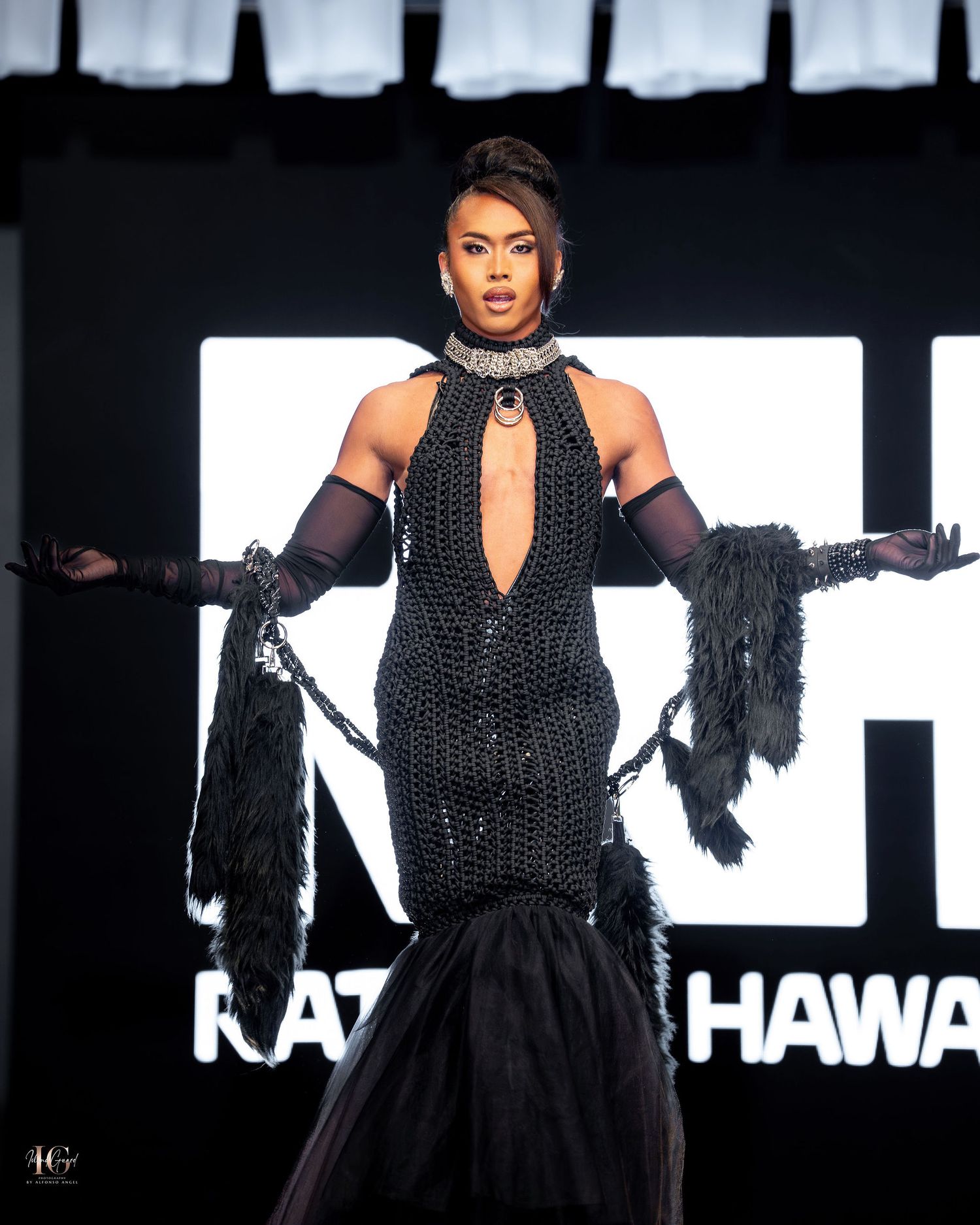 Model in a black halter dress with polka dots performs on stage with dramatic lighting and feathered props.