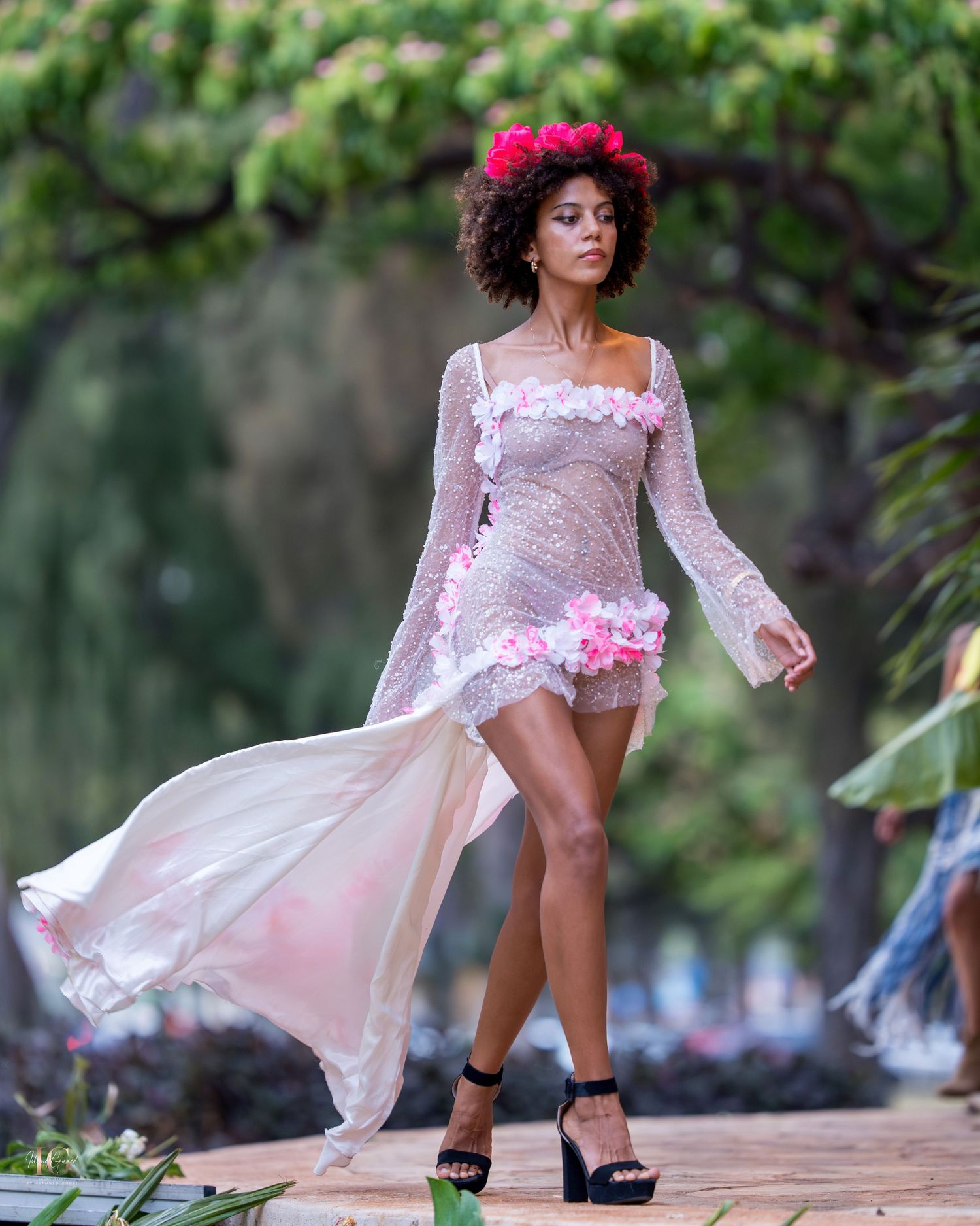 A dancer in a flowing pink dress performs graceful movements outdoors in a natural garden setting.