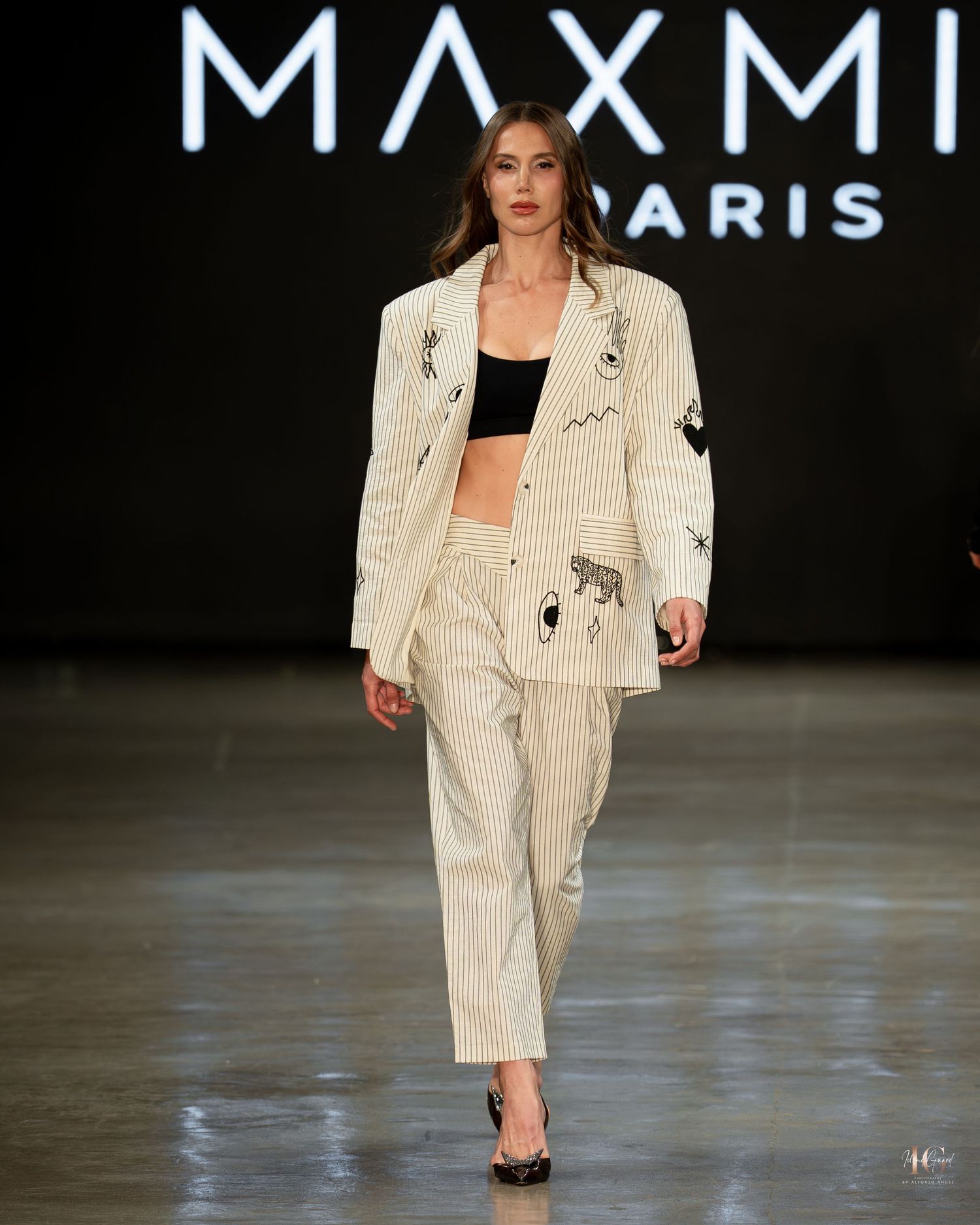 Model walks runway in cream pinstriped suit during fashion show presentation.