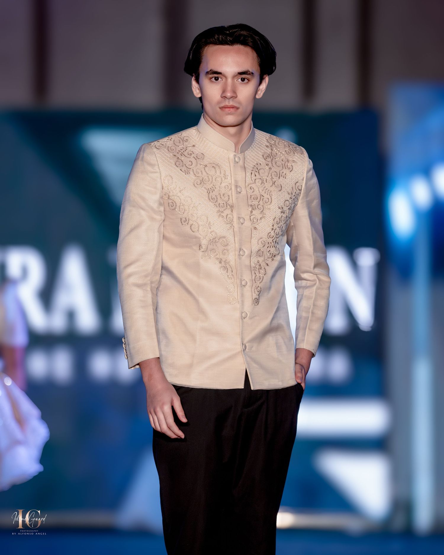 Model presents cream embroidered jacket with dark trousers on contemporary fashion runway.