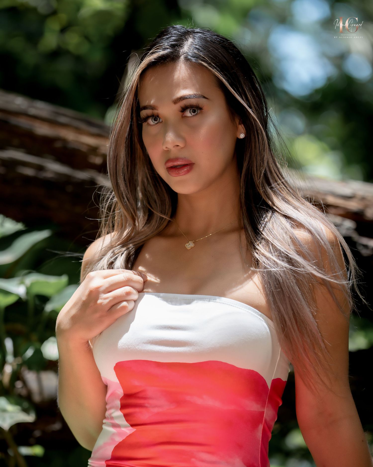 Person in a white and coral strapless dress poses in natural outdoor lighting against greenery in the background.