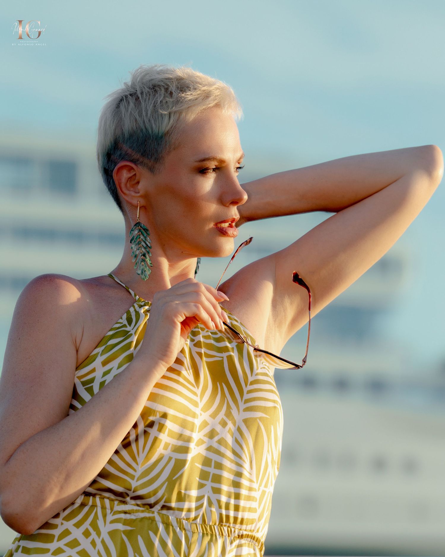 A person in a yellow and black striped summer dress poses against a blurred outdoor background in warm sunlight.