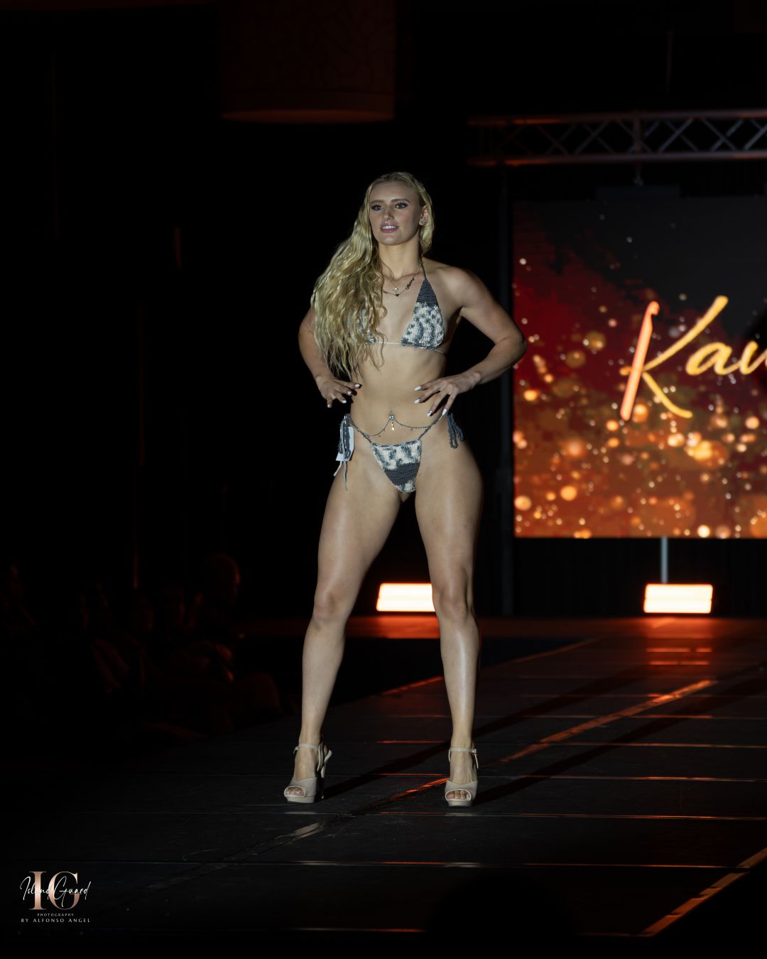 Model strikes pose on catwalk during swimsuit segment of fashion show.