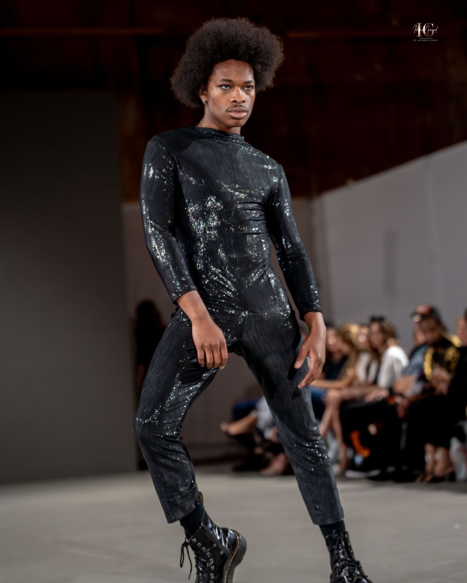 Model walks runway in distressed black denim and matching jacket during fashion show presentation.