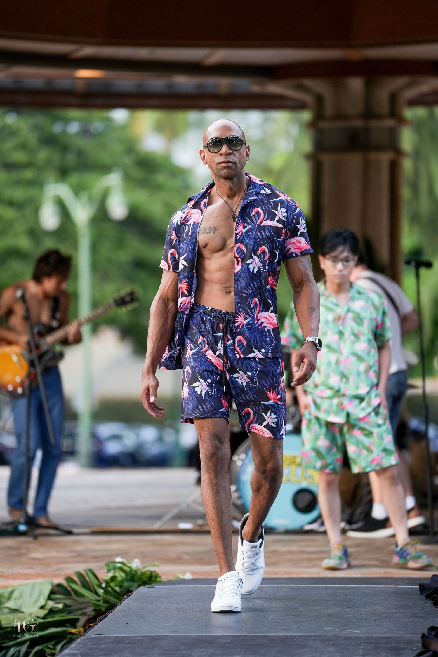 Person in blue floral shirt and white shoes performs energetic dance moves on concrete surface in outdoor setting.