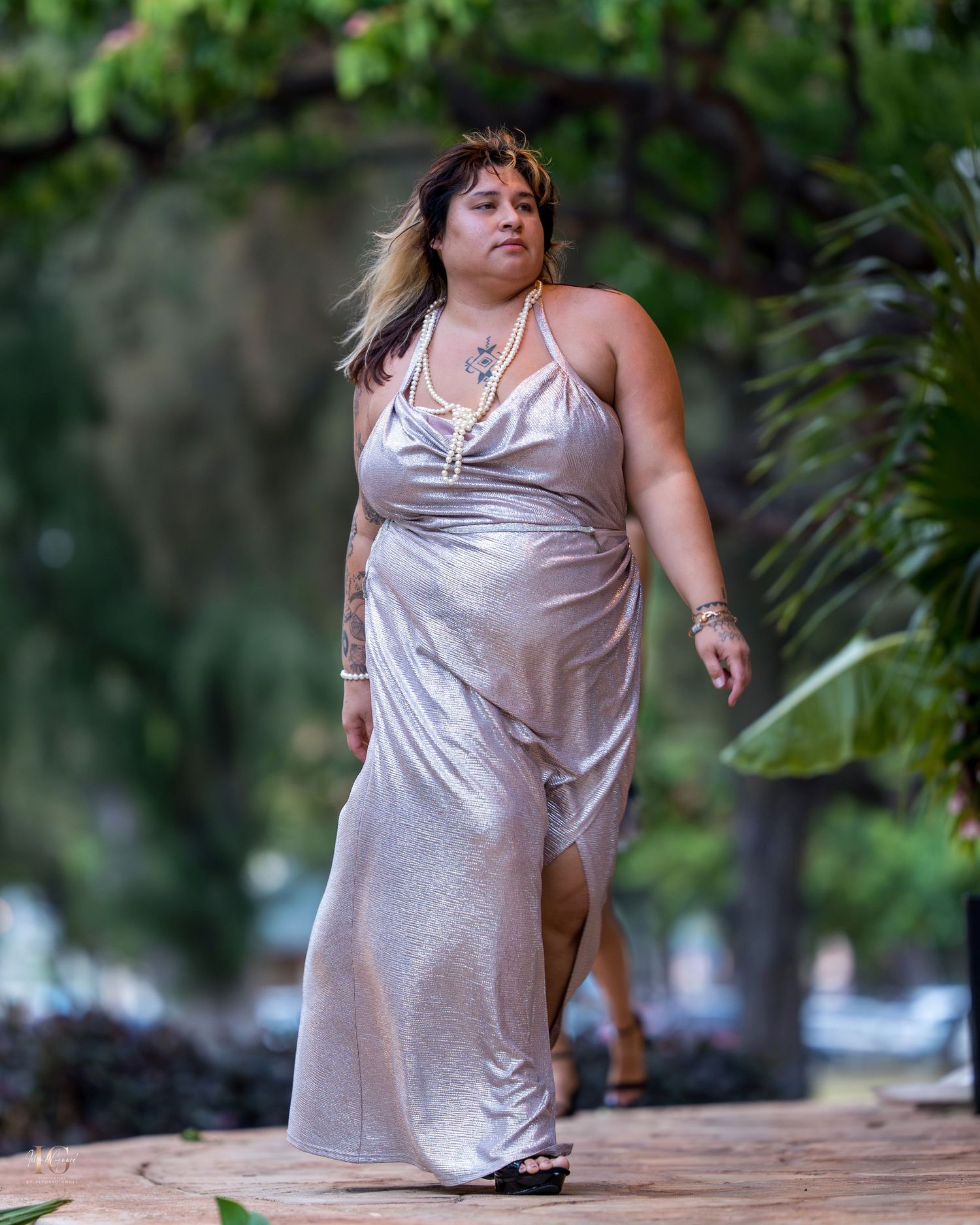 A person wearing a light-colored satin dress poses in a natural outdoor setting with trees in the background.