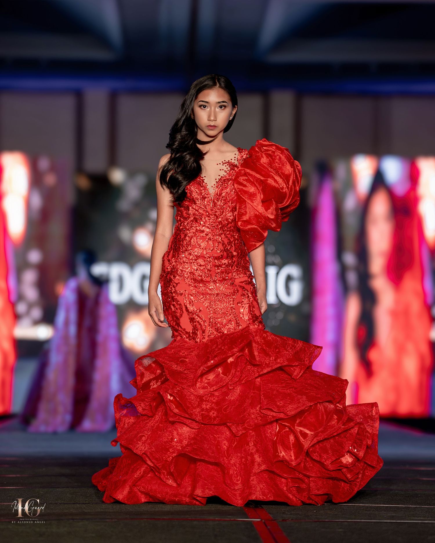 Dramatic red ruffled gown with textured fabric shown on illuminated catwalk.