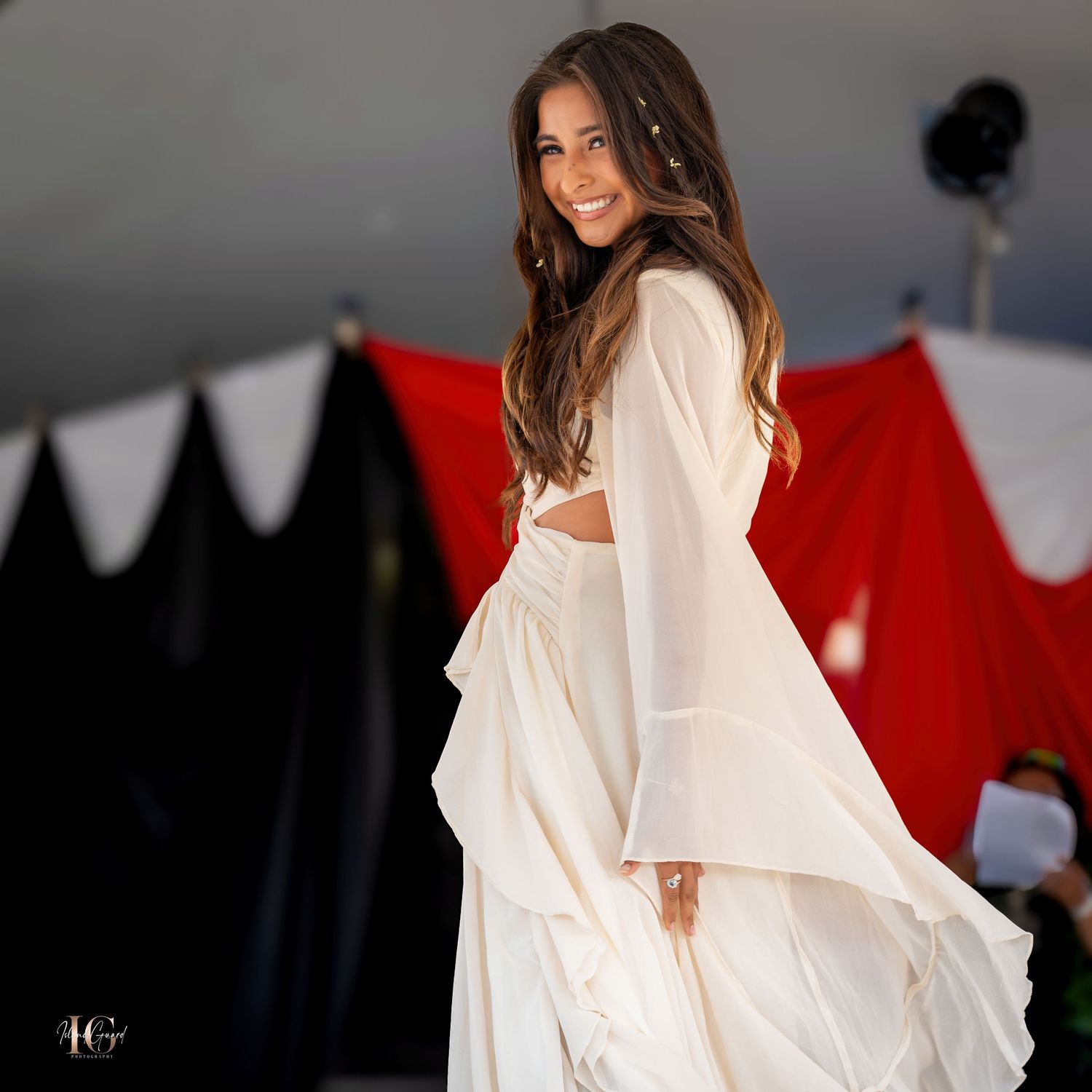 Fashion portrait featuring flowing white garment against dramatic red and black background.