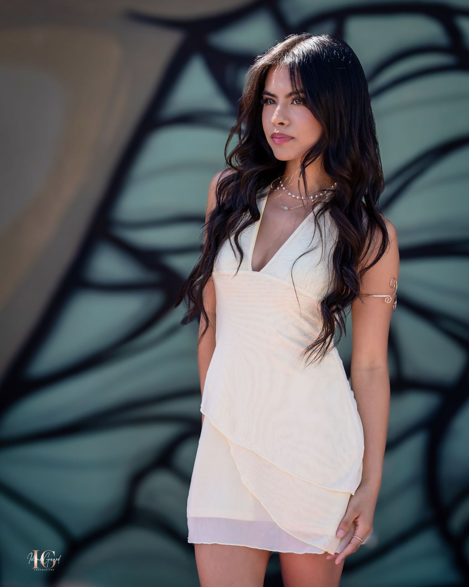 Model in white mini dress poses elegantly against turquoise mural backdrop.