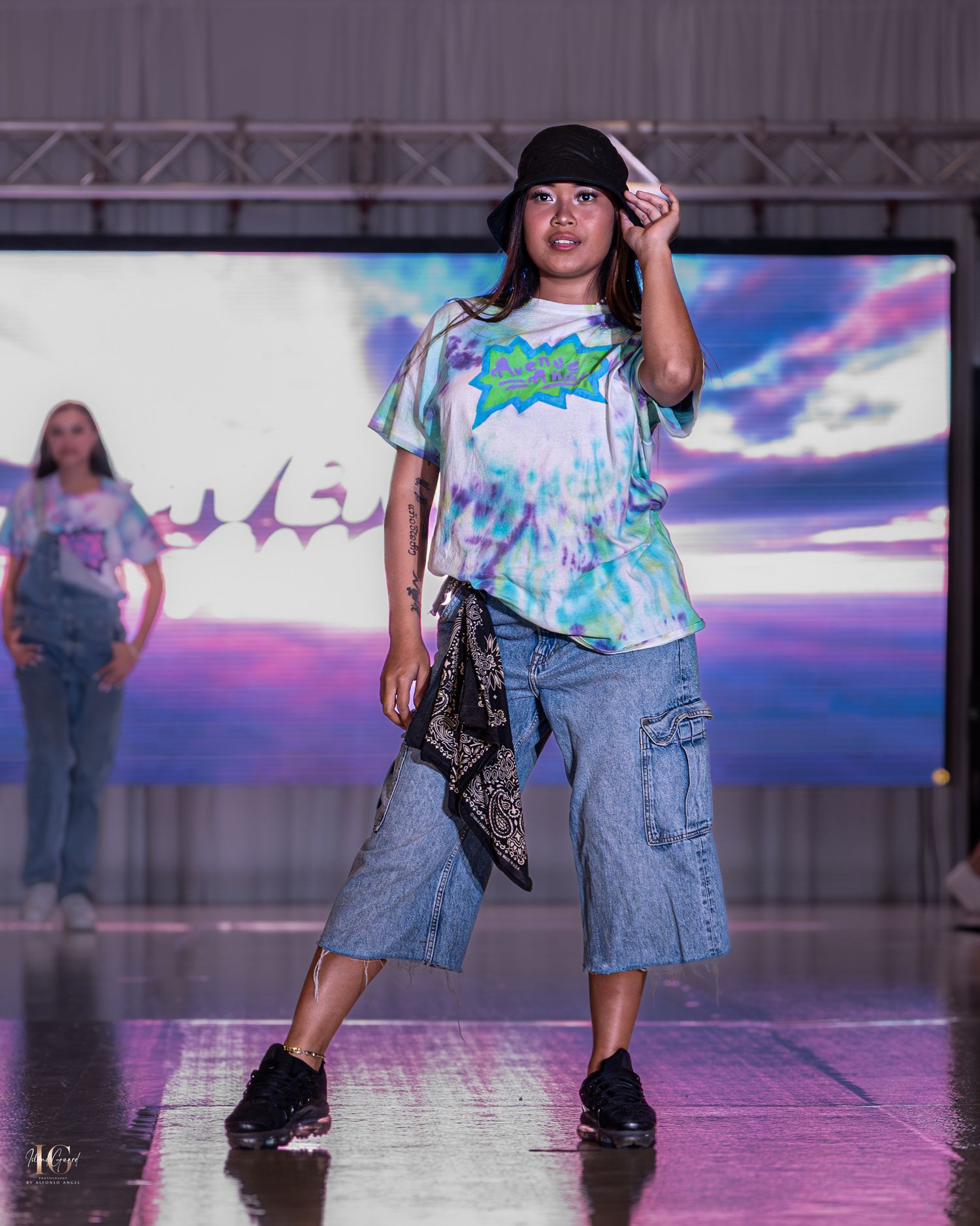 Models showcase casual denim outfits with tie-dye tops on a fashion runway with colorful lighting effects.
