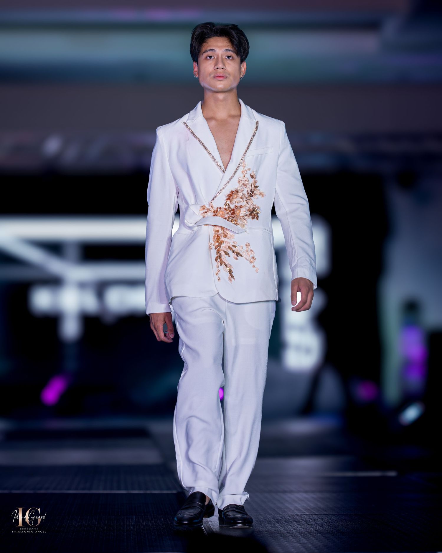 White embellished suit with floral accent detail showcased during evening fashion show.