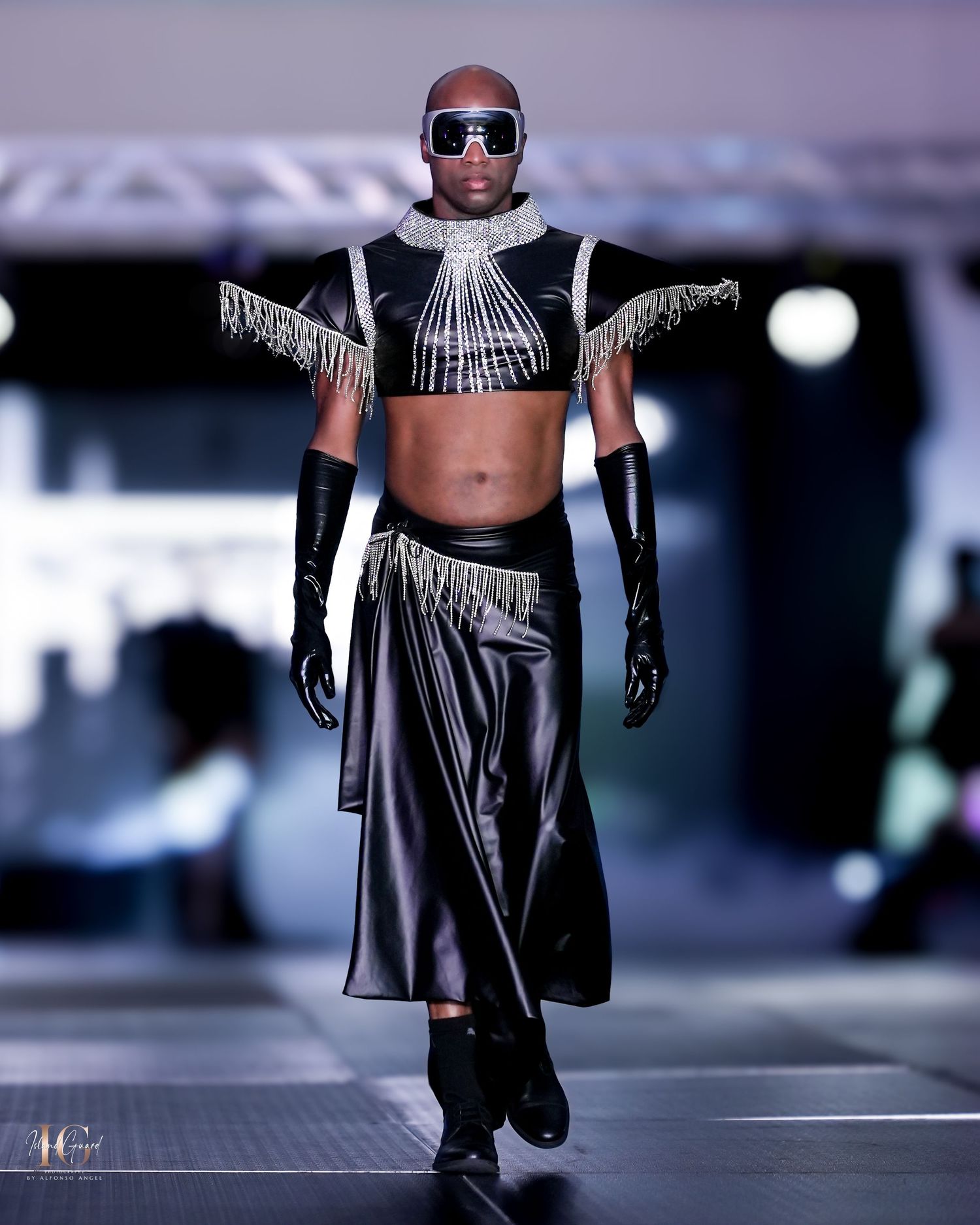 Model in avant-garde black and silver crop top with fringe details and flowing skirt on runway.