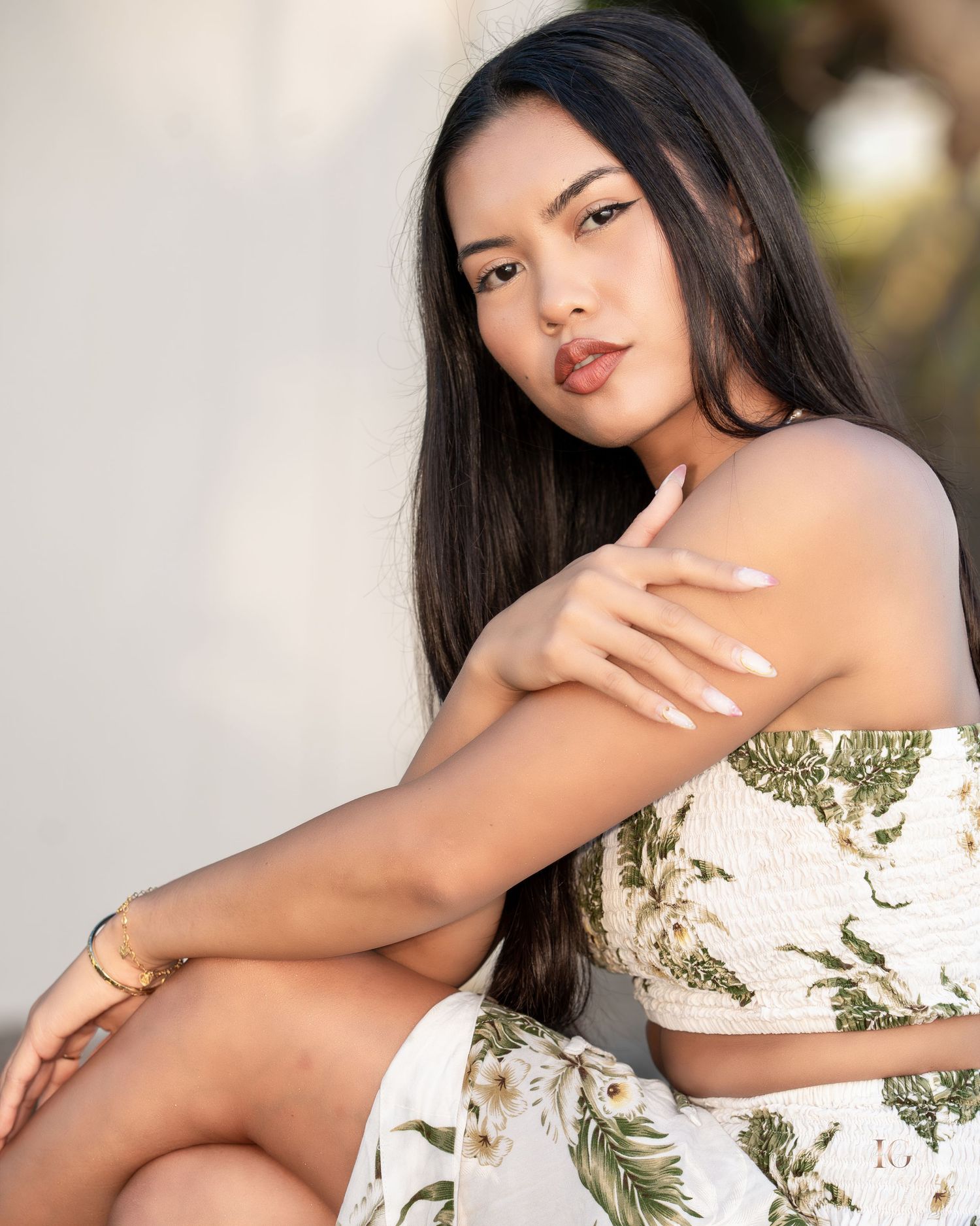 A woman in white attire poses elegantly against a soft neutral background with floral elements.