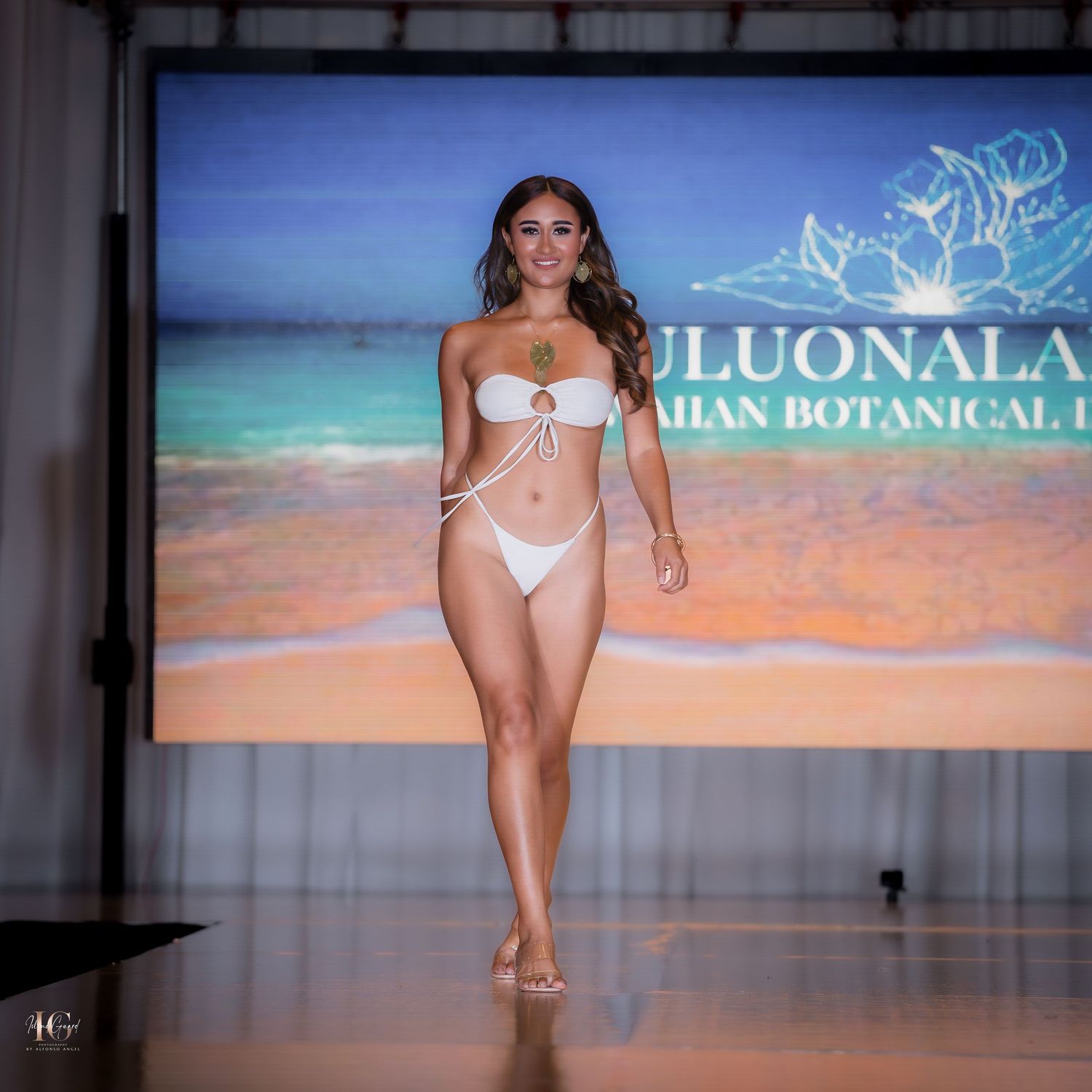 Model showcases white bikini on beach-themed runway for Luonala collection.