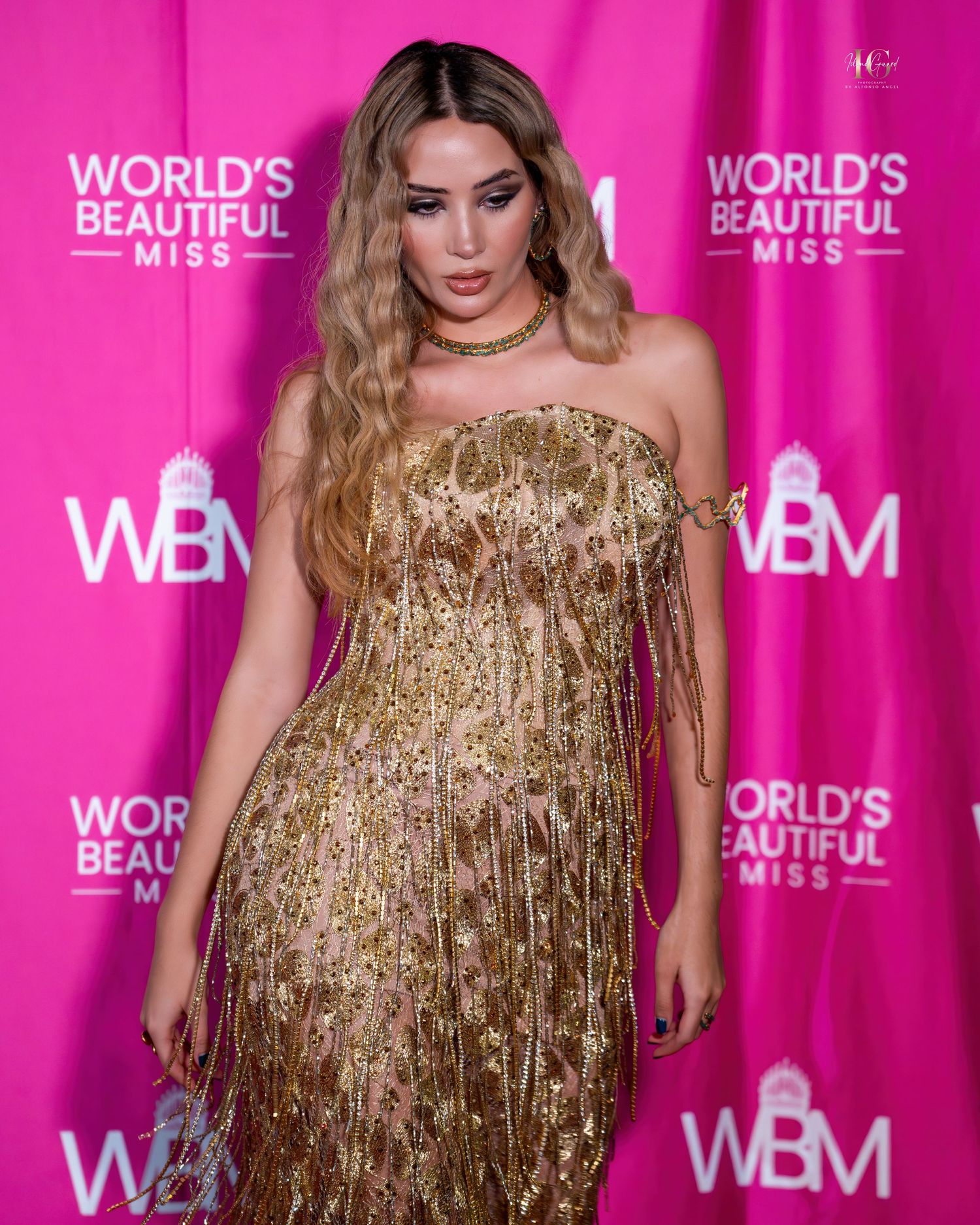 Model in shimmering gold strapless gown poses at World's Beautiful Miss event.
