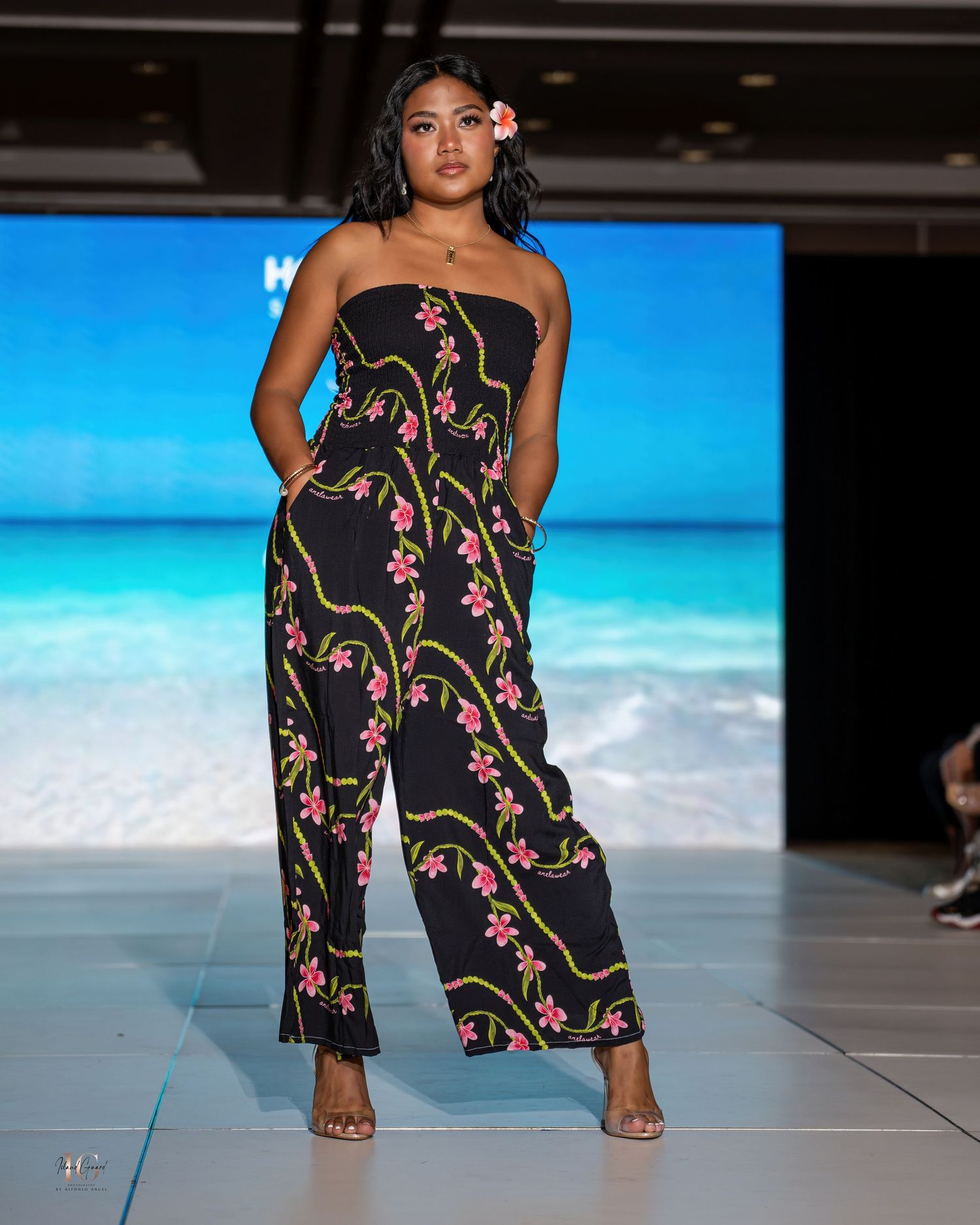 Model presents black floral jumpsuit with pockets during beachwear fashion show.