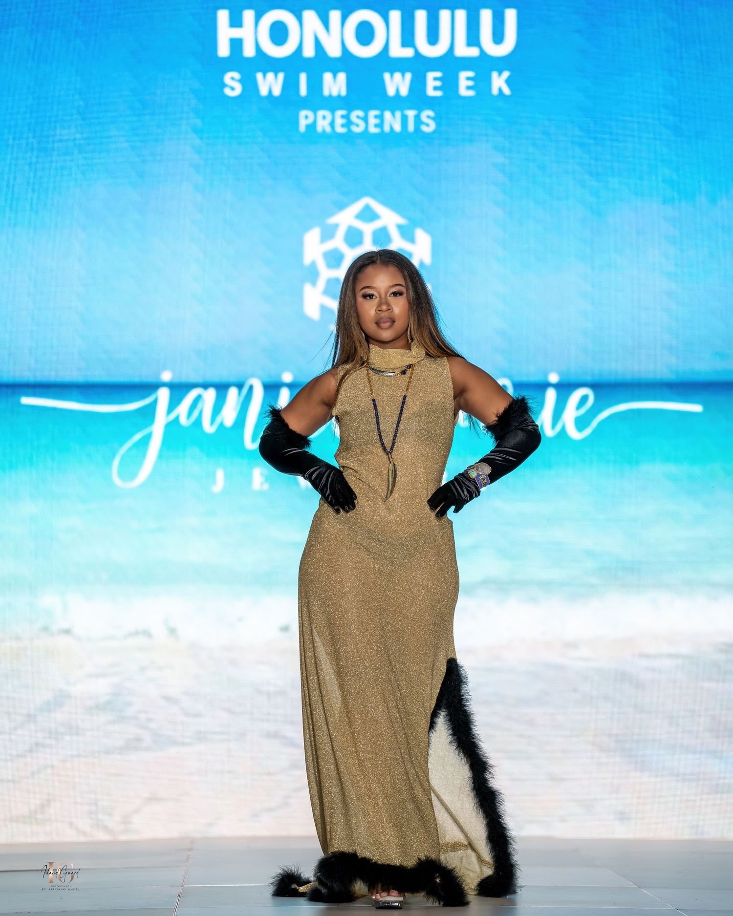 Model wearing beige long dress and gloves on runway at Honolulu Swim Week fashion show.