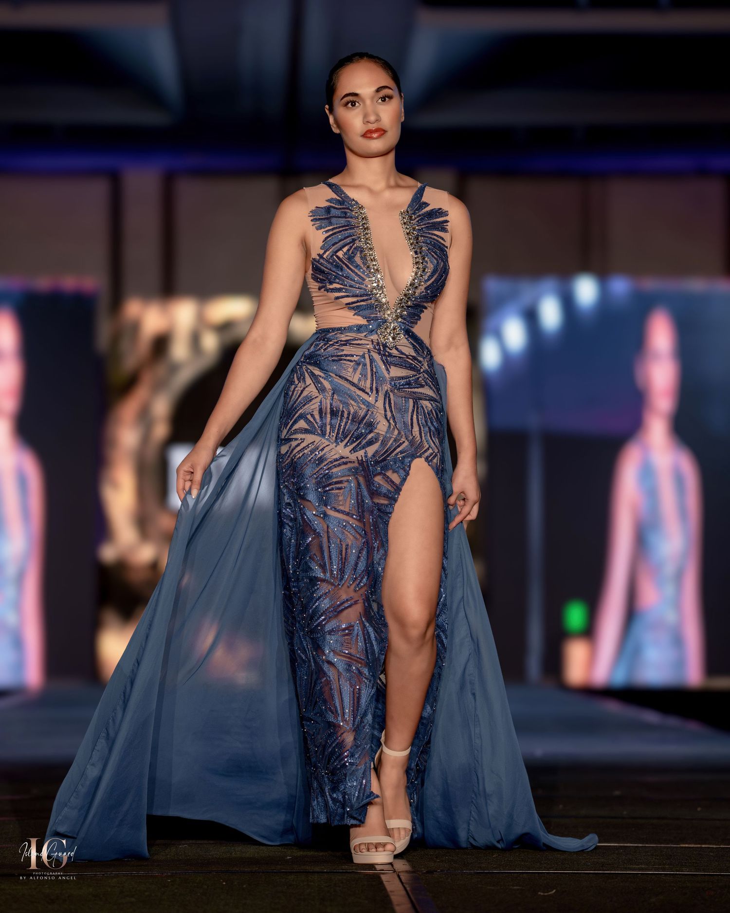 Blue high-slit gown with cutout details and flowing train on fashion runway.