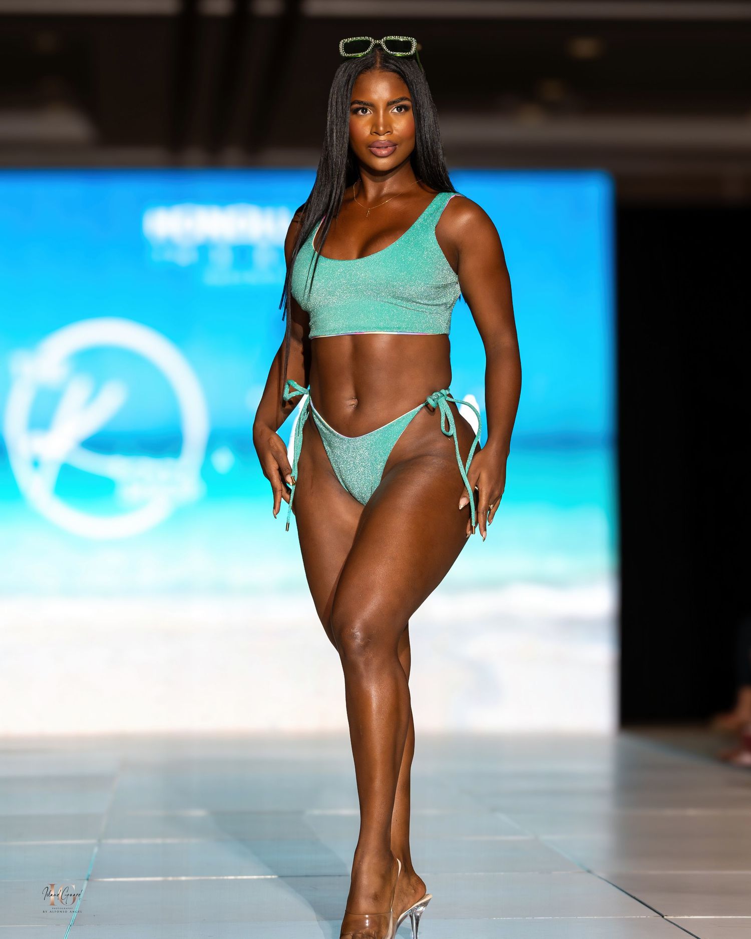 Models present mint green swimsuits during beach-themed runway show.
