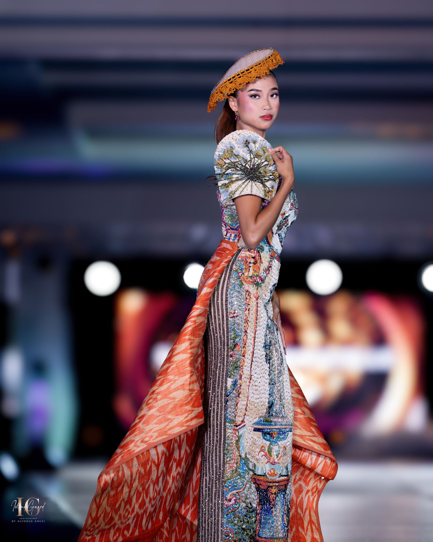 Elegant evening wear with orange cape and silver embellishments presented on professional catwalk.