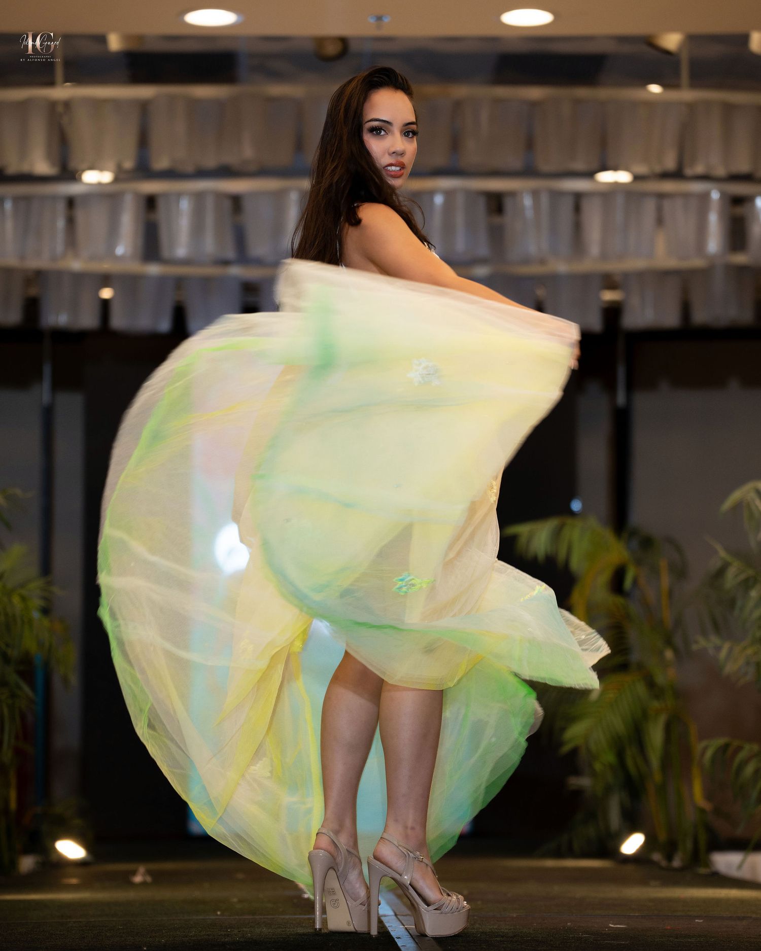 Model wearing a flowing yellow-green dress twirls on a runway with dramatic fabric movement.