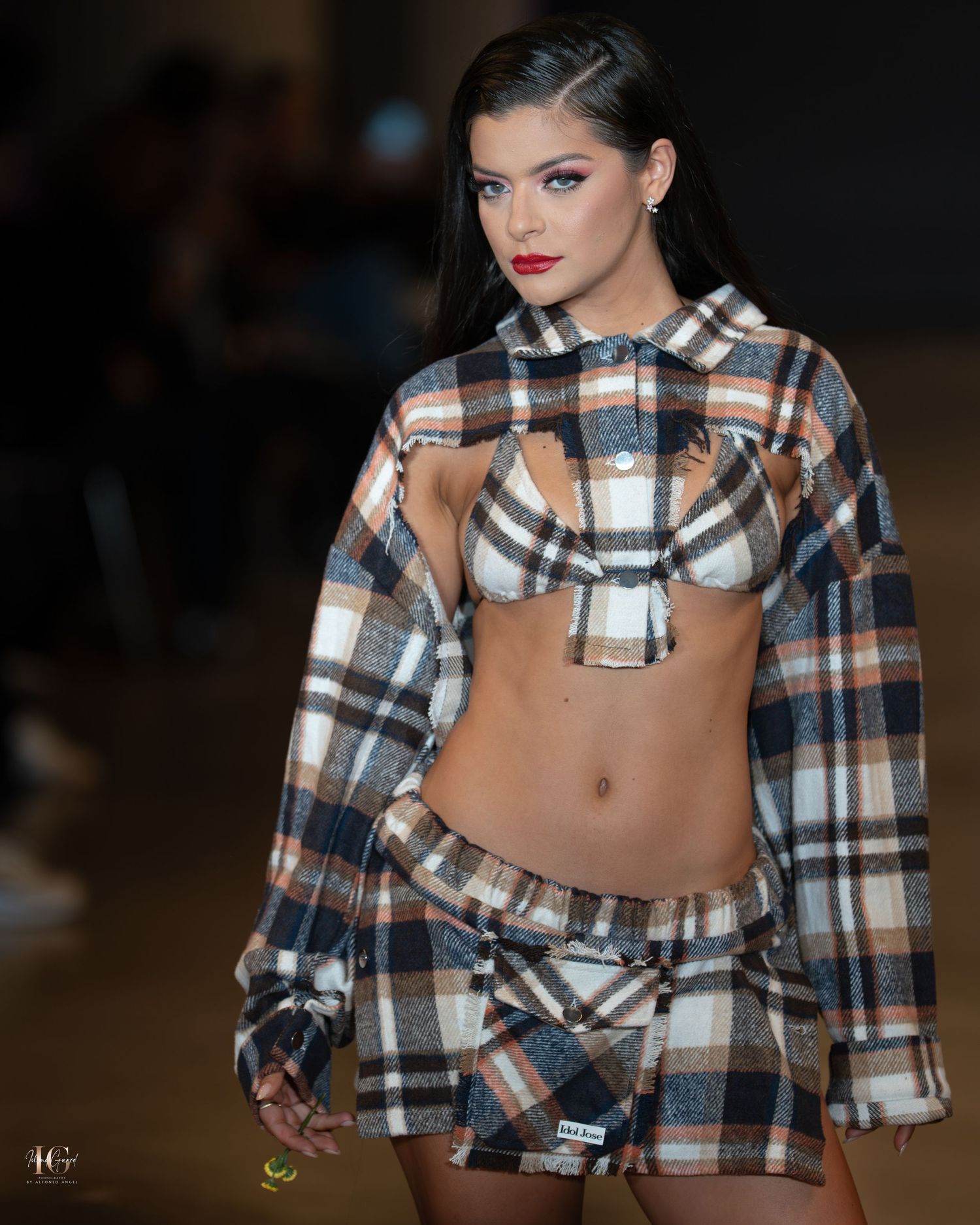 Model walks runway in cropped plaid jacket and low-rise pants during fashion show presentation.