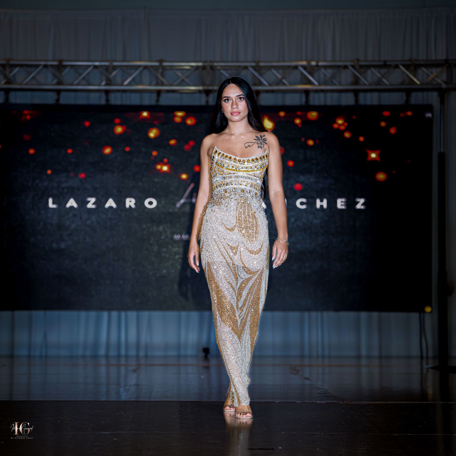 Sequined gold evening gown presented on fashion runway with dark background.