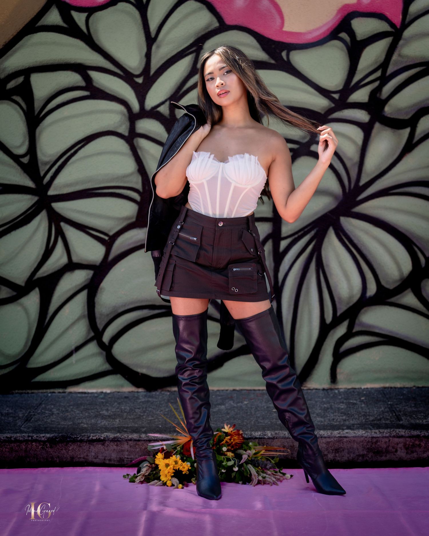 Fashion model poses against graffiti wall in black outfit with white top and knee-high boots.